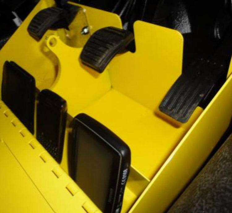 Close-up of a bright yellow vehicle  footwell area lock box with black foot pedals and mobile phones stored.